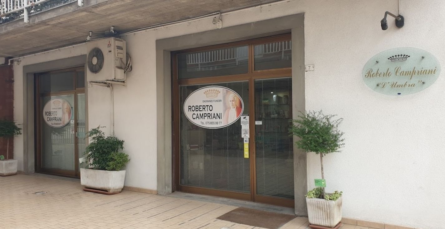 Ingresso di Onoranze Funebri Roberto Campriani con vetrine in legno, insegna ovale «L'Umbra» e piante in vasi bianchi